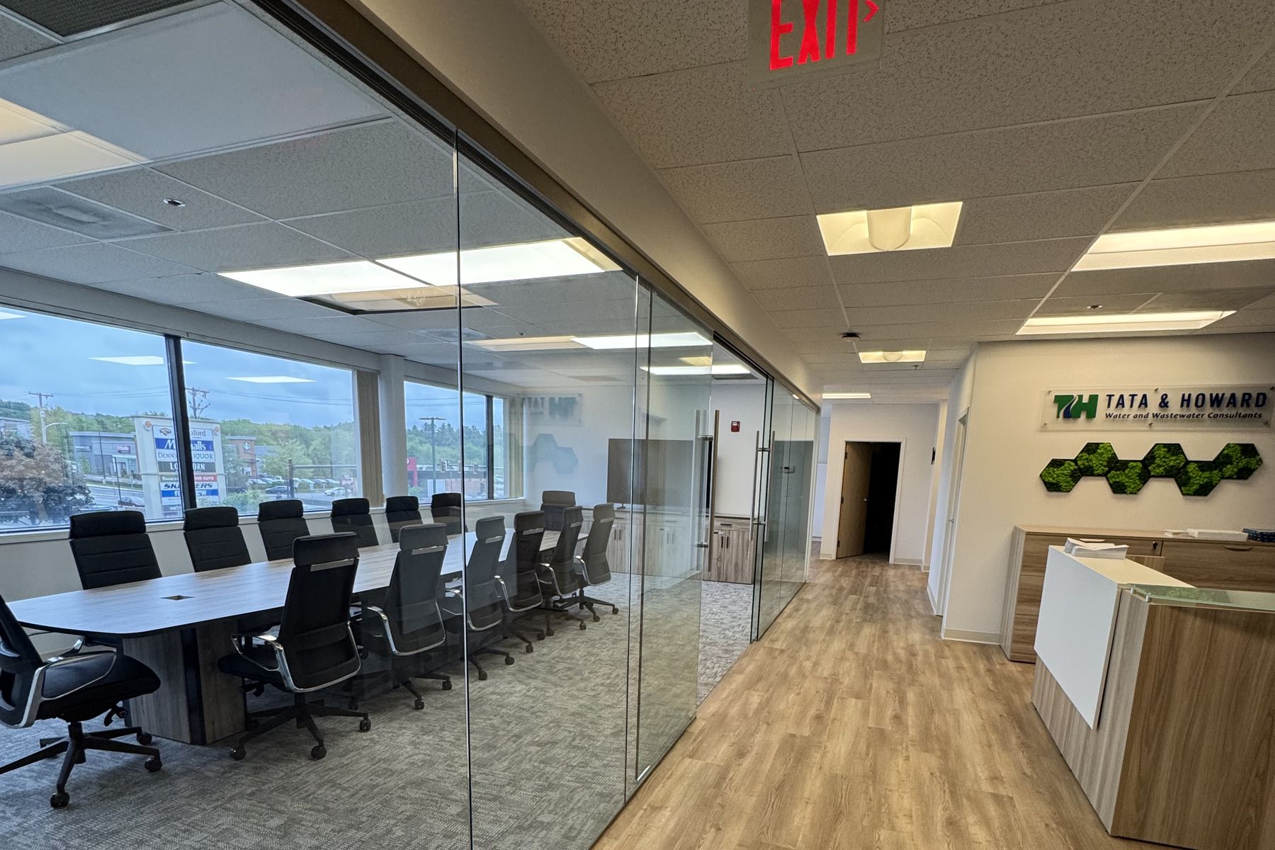 Glass-walled conference room and reception desk installed by Commercial Office Interiors at Tata & Howard in Marlborough, MA, with a preserved-moss feature wall behind the reception desk